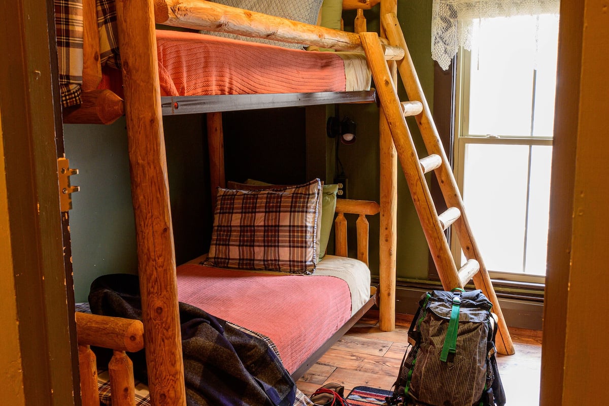 A bunk bed room with a wooden ladder, a small table, and a backpack on the floor.