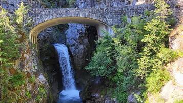 A stone bridge arching over a waterfall with lush greenery on either side.