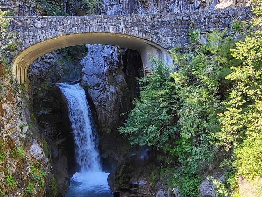 A stone bridge arching over a waterfall with lush greenery on either side.