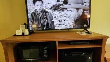 Un televisor sobre un soporte de madera, un control remoto, un microondas y un refrigerador pequeño.