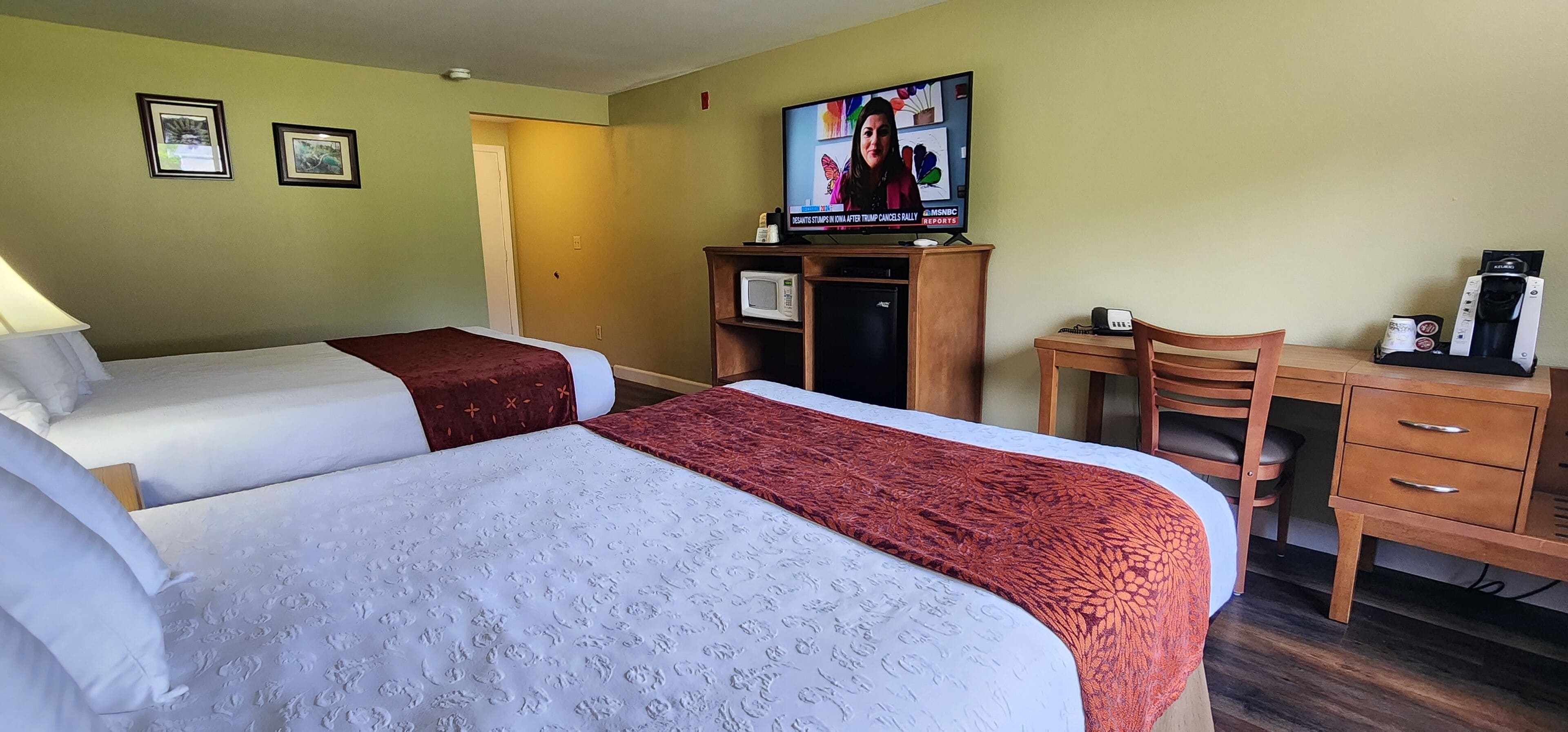 A hotel room with two beds, a desk, a chair, a television, and a coffee maker.