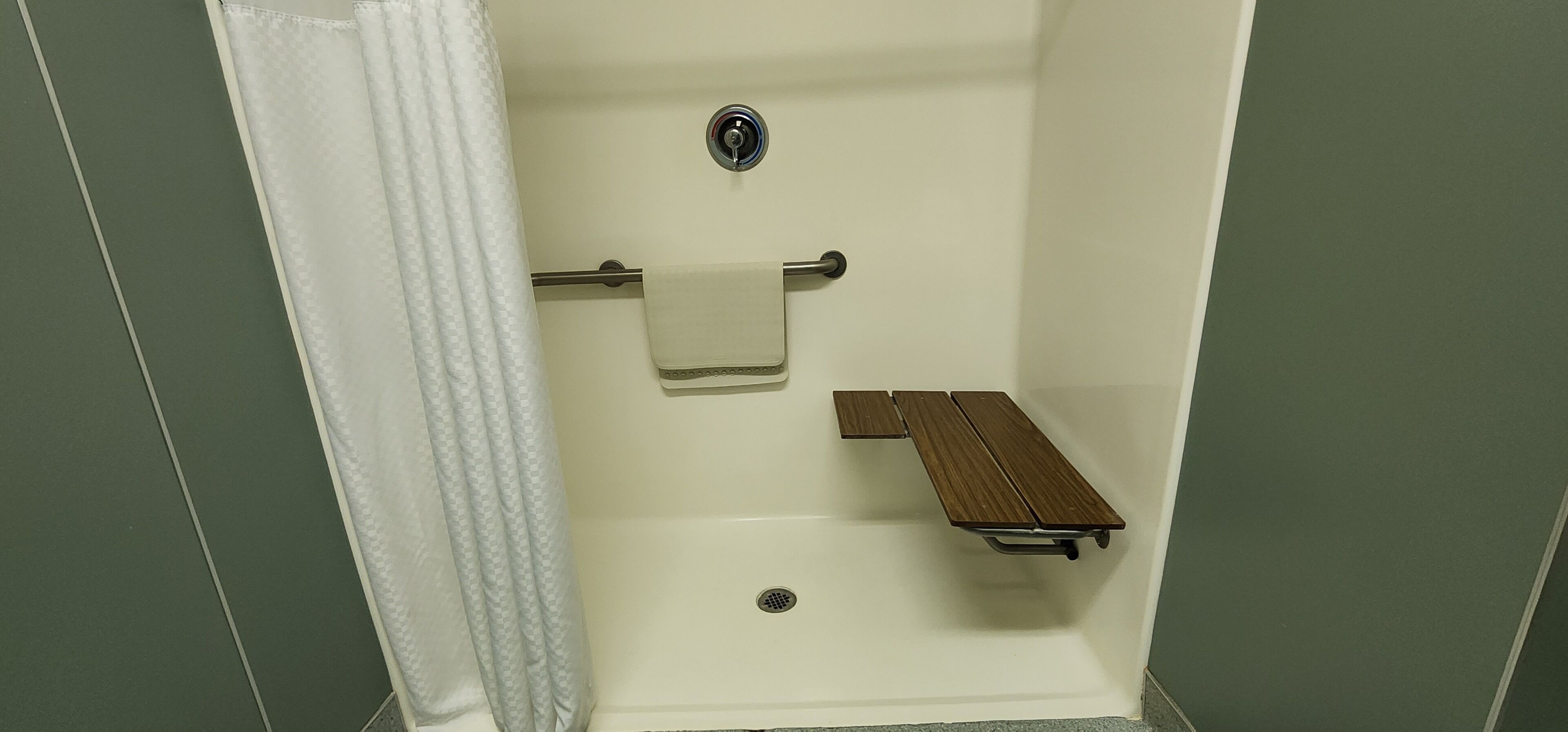 A shower with a towel rack, a bench, and a drain.