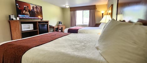 Une chambre d’hôtel avec deux lits, un bureau équipé d’un ordinateur, un four à micro-ondes et un téléviseur diffusant un programme d’information.