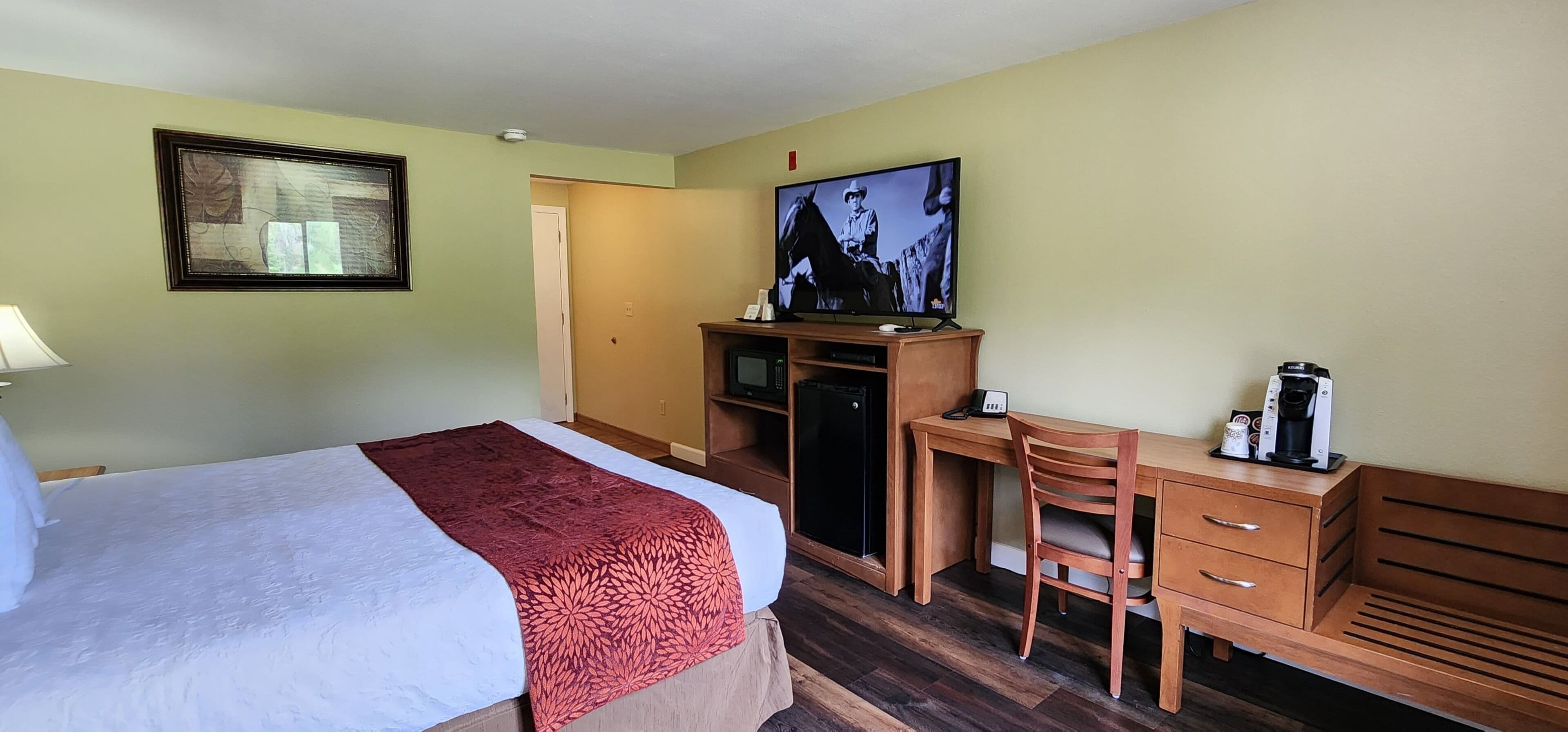 A hotel room with a bed, a desk, a chair, a television, and a coffee maker.