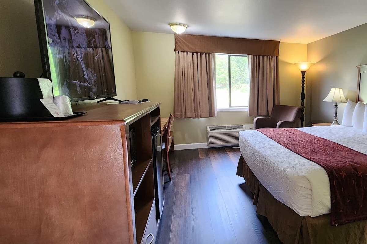 A hotel room with a large bed, a desk with a computer, a chair, a window with curtains, and a lamp.