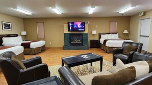 Habitación de hotel con dos camas, televisión, chimenea, asientos de cuero y una mesa de centro.