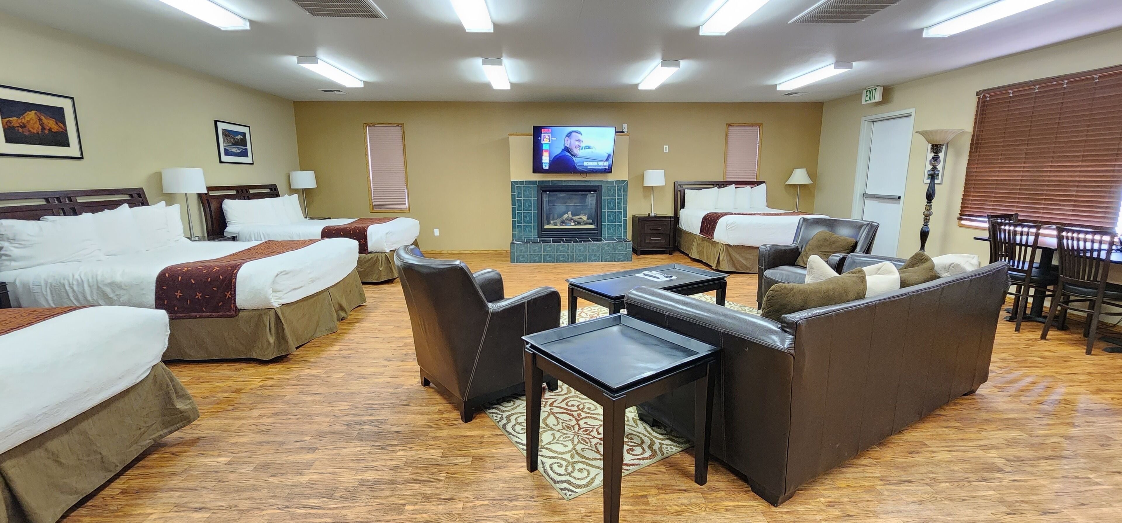A hotel room with two beds, a sofa, a TV, a fireplace, and a dining area.