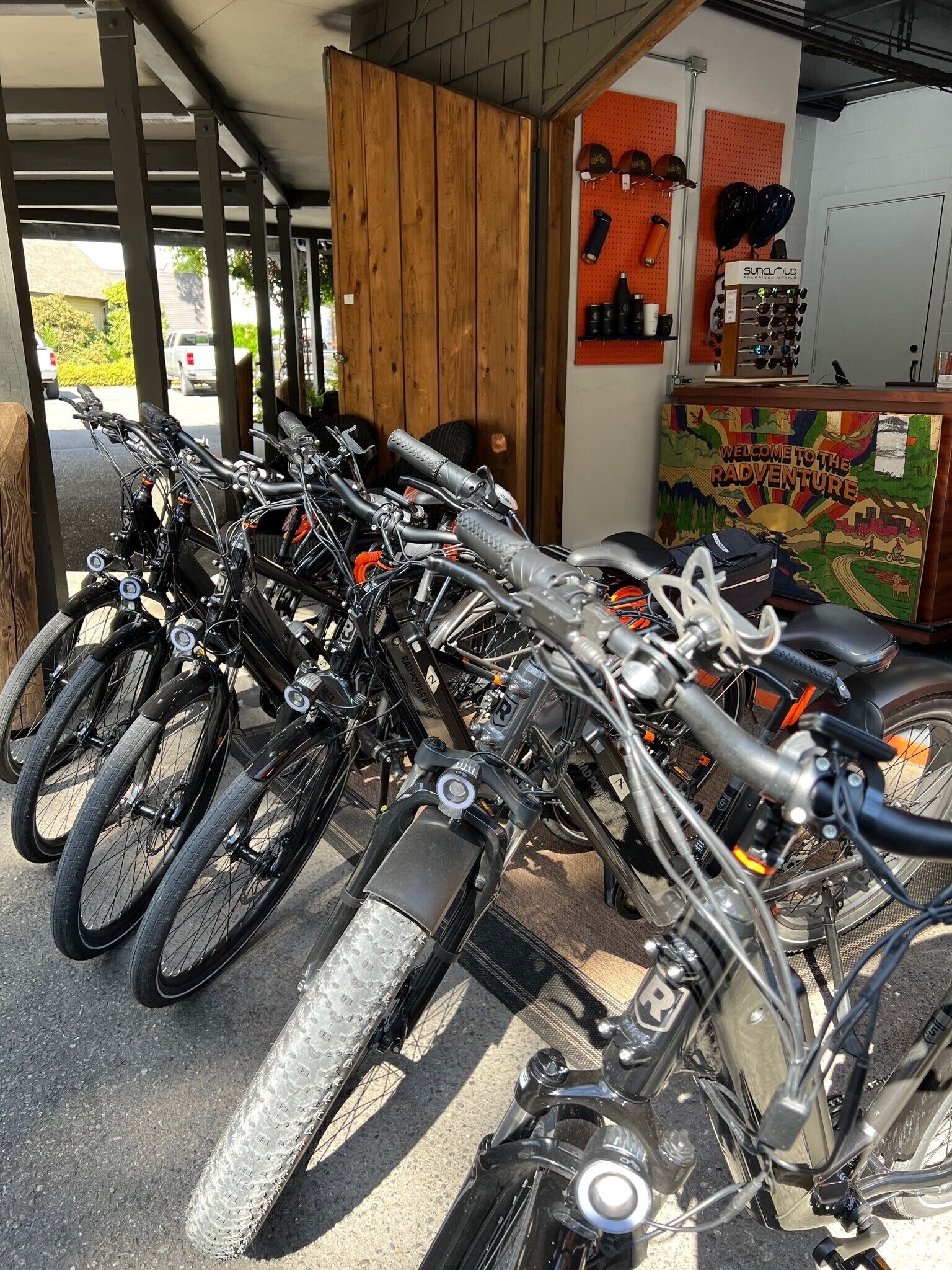 A row of bicycles parked under a covered area with a wooden wall and a colorful mural in the background.