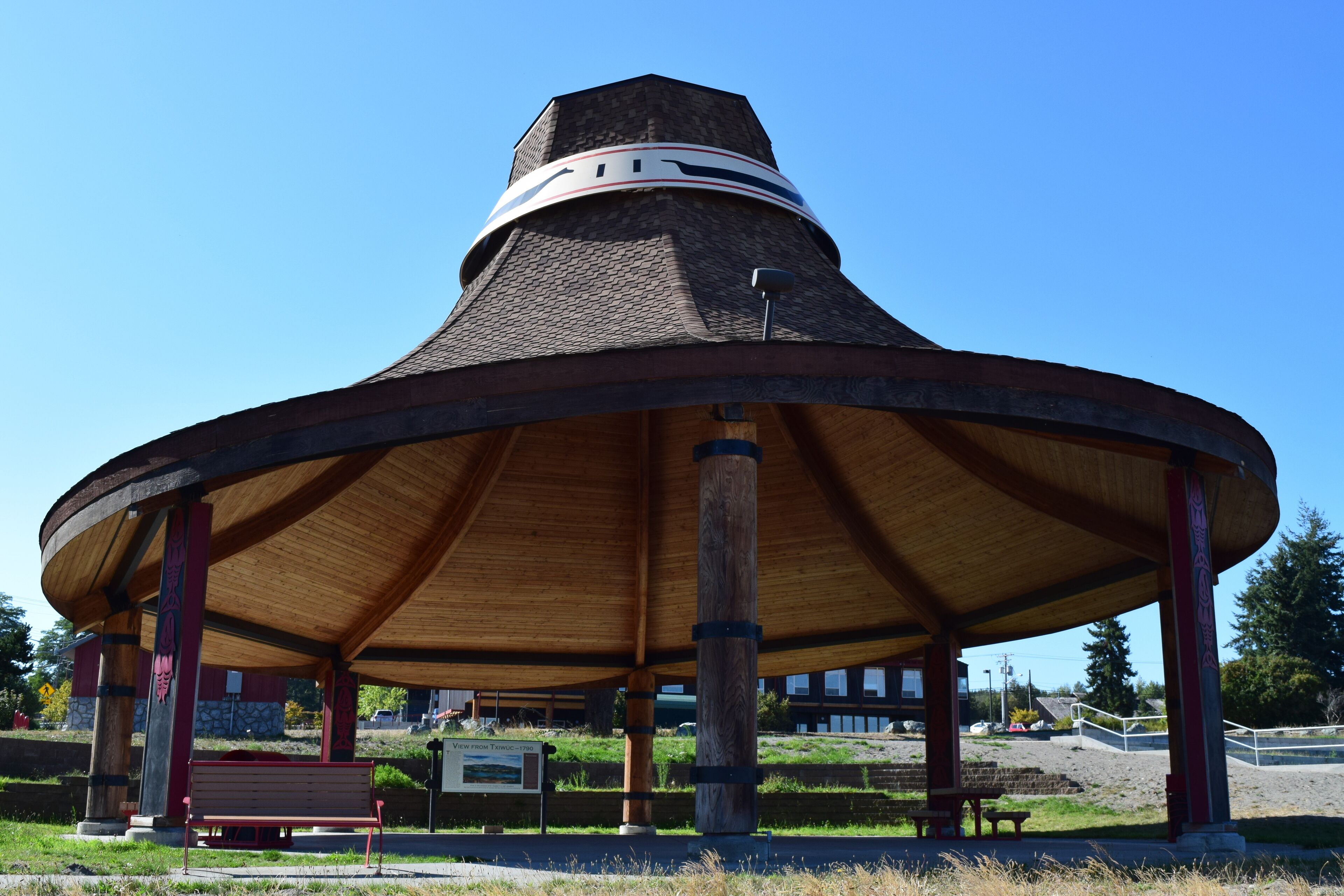 A wooden pavilion with a conical roof, benches, and a sign.