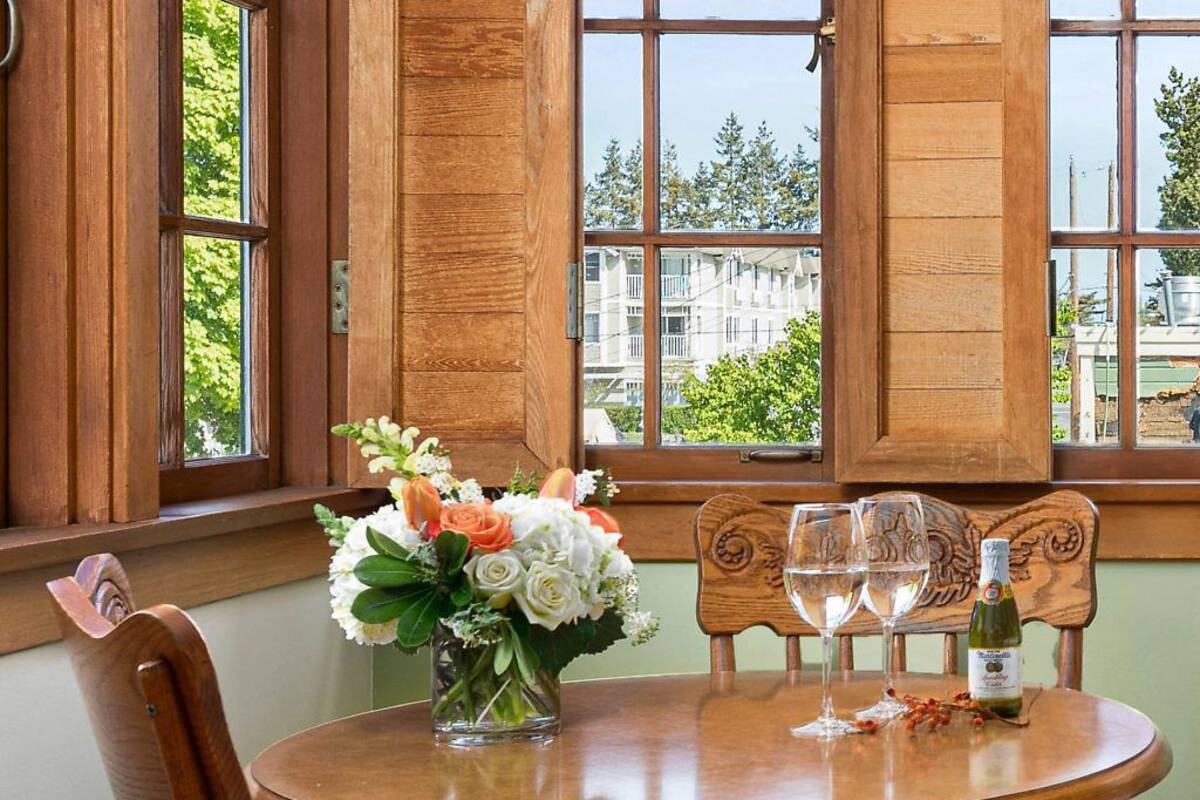 A wooden dining table with a vase of flowers, two wine glasses, and a bottle of wine.