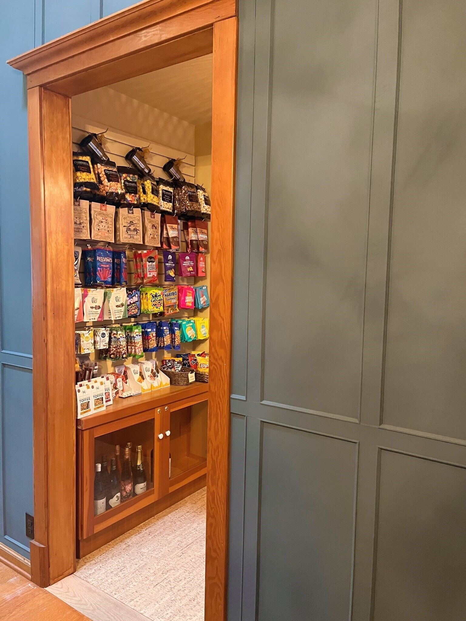 A narrow hallway with a wooden cabinet filled with various packaged snacks and a glass cabinet with bottles.
