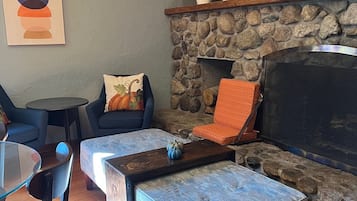 Ein gemütliches Wohnzimmer mit Kamin aus Stein, einem blauen Sofa, einem Couchtisch und einem Essbereich mit Glastisch und Stühlen.