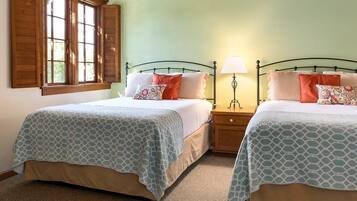 A room with two beds, each with a patterned bedspread, a nightstand with a lamp, and a window with wooden shutters.