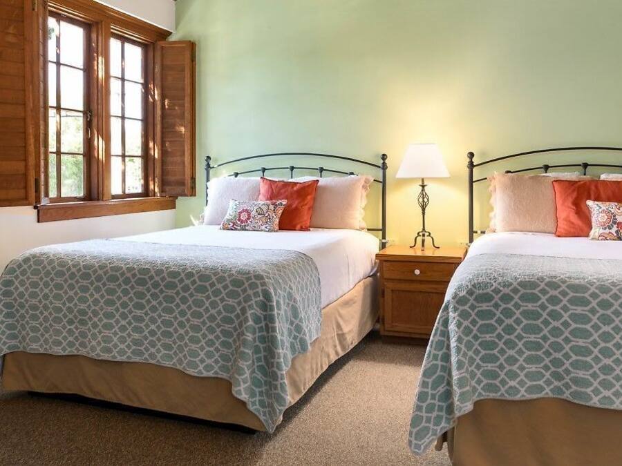 A room with two beds, each with a patterned bedspread, a nightstand with a lamp, and a window with wooden shutters.