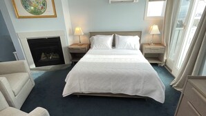 Une chambre d’hôtel avec un grand lit, deux tables de chevet avec des lampes, une cheminée et une grande fenêtre avec des rideaux.