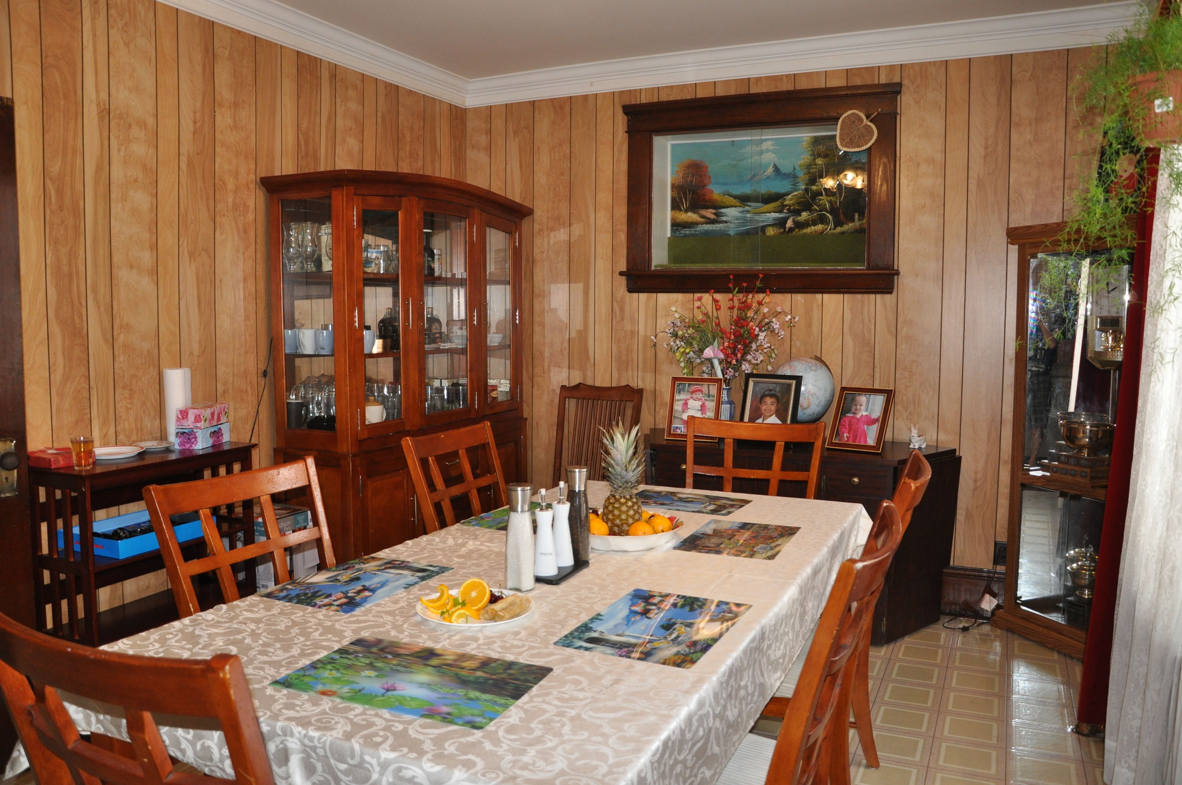 Un coin repas avec des lambris en bois, un grand tableau au-dessus de la table et un buffet aux portes vitrées.