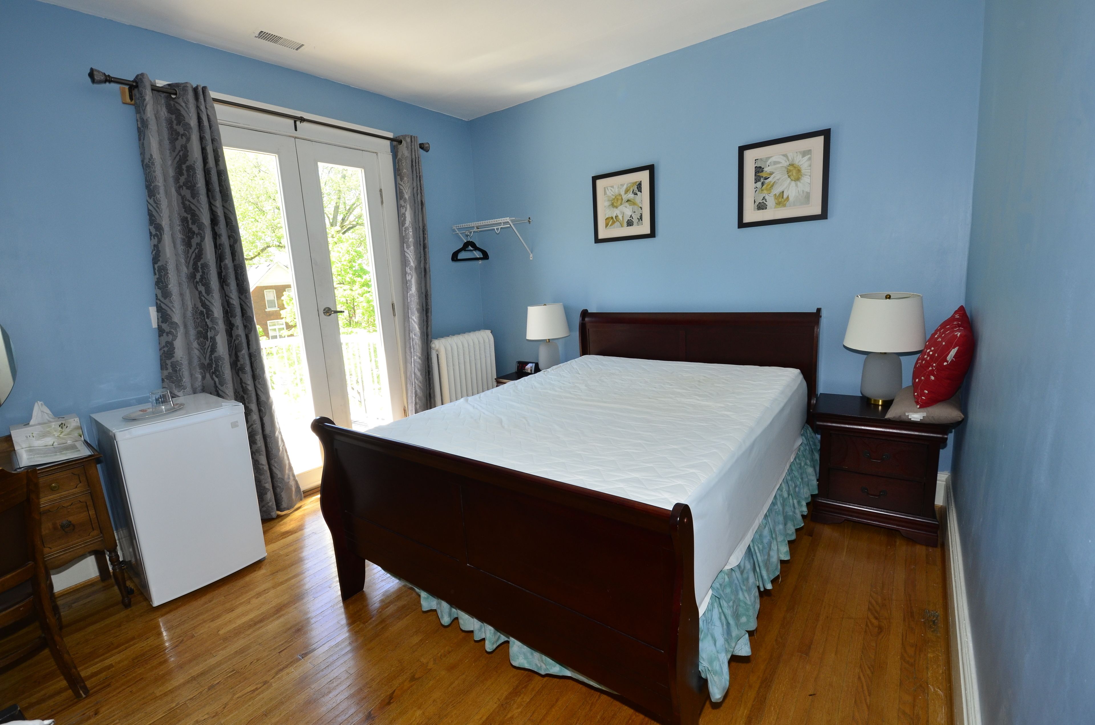 Un dormitorio con una cama de madera, dos mesitas de noche con lámparas, un electrodoméstico pequeño y un ventanal con cortinas.