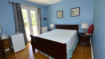 Un dormitorio con una cama de madera, dos mesitas de noche con lámparas, un electrodoméstico pequeño y un ventanal con cortinas.