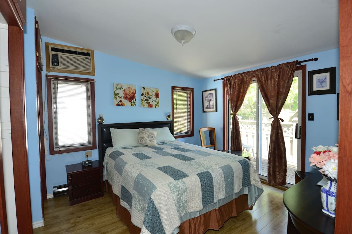 A bedroom with a bed, a nightstand, a dresser, a window with blinds, and a door.