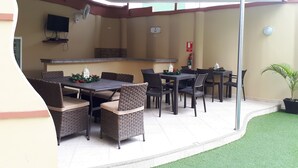 An outdoor dining area with wicker chairs and a table, a flat-screen TV mounted on the wall, and a fire extinguisher. - Hotel Avellán (Manta)