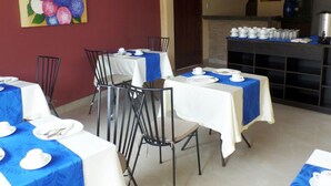 A dining area with tables set for service, a kitchen area with appliances, and a painting on the wall. - Hotel Avellán (Manta)
