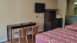A hotel room with a desk, two chairs, a television mounted on the wall, a microwave, and a bed with patterned bedding. - Western Inn (Union City)