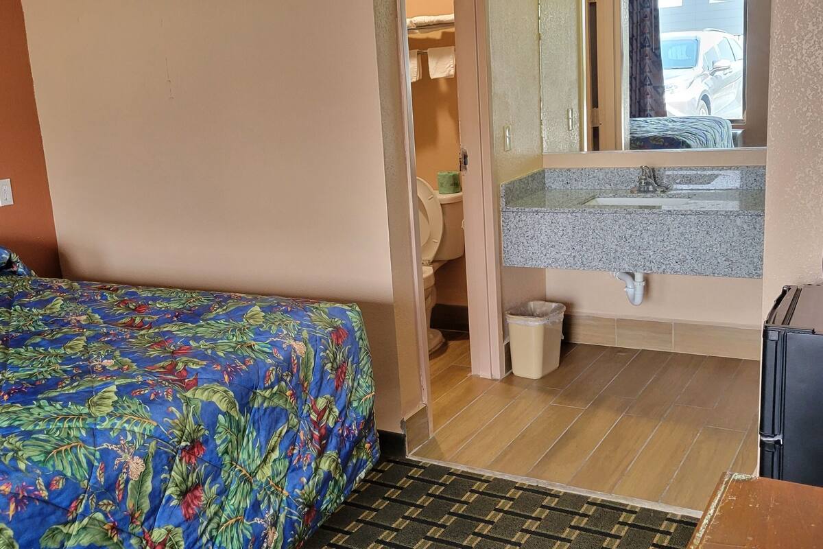 Ett hotellrum med en säng, ett handfat, en spegel och ett kylskåp.
