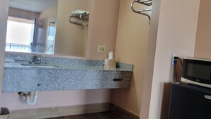 A bathroom with a granite countertop, a sink, a mirror, a towel rack, a microwave, and a refrigerator. - Western Inn (Union City)