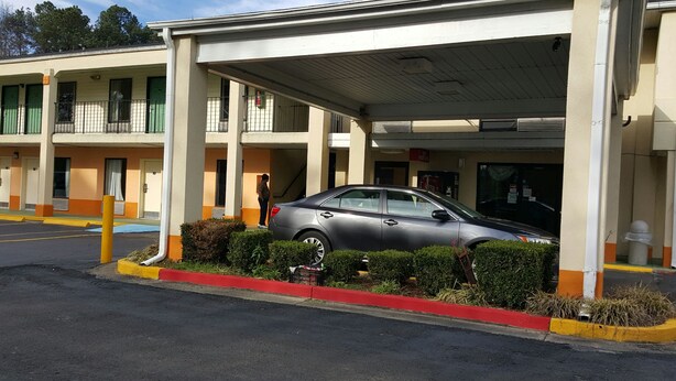 A motel with a covered parking area, a car parked inside, and a person standing near the entrance. - Western Inn (Union City)