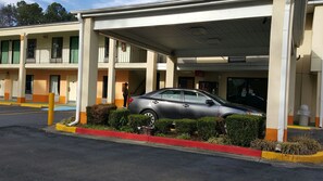 A motel with a covered parking area, a car parked inside, and a person standing near the entrance. - Western Inn (Union City)