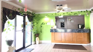 A reception area with a green wall, a wooden counter, and a ceiling fan. - Western Inn (Union City)