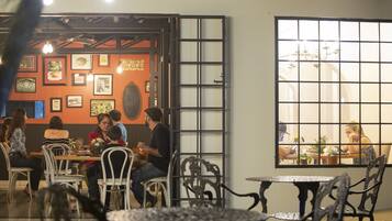 An indoor dining area with tables and chairs, framed pictures on the walls, and a large window with a view of another dining area.