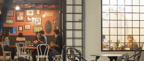 An indoor dining area with tables and chairs, framed pictures on the walls, and a large window with a view of another dining area.