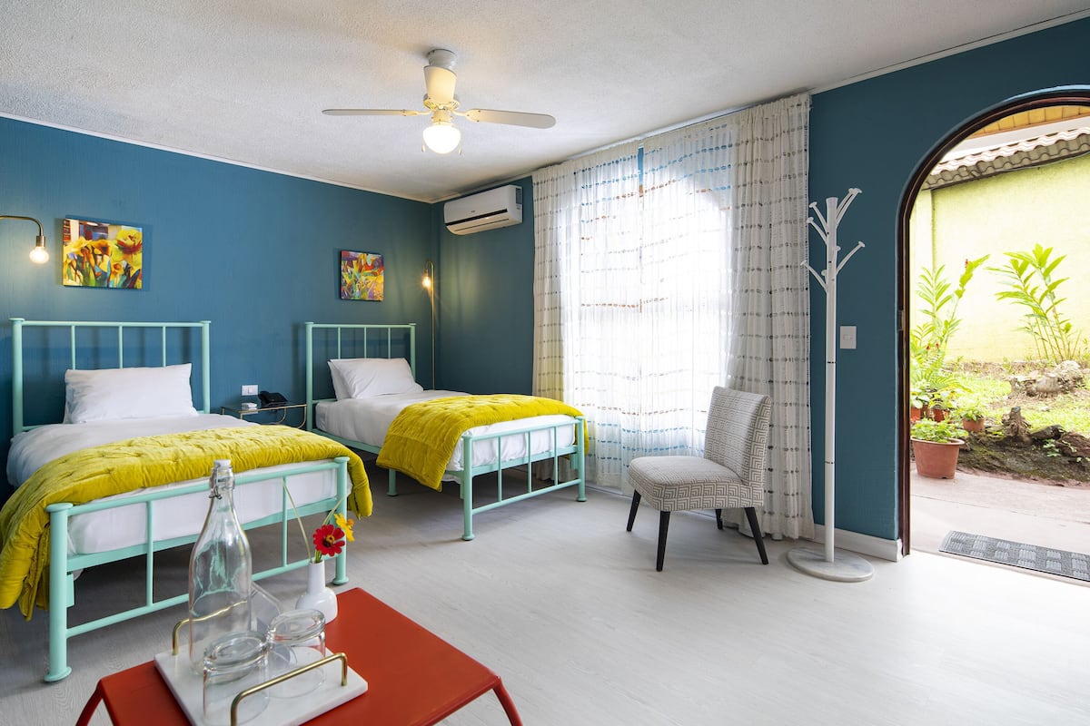 A room with two beds, a chair, a table, and a ceiling fan.