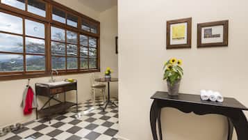 Una habitación con piso de cuadros, una ventana con vistas, un escritorio con un florero y cuadros en la pared.