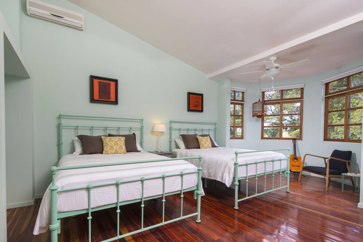 A room with two beds, a guitar, a chair, and framed pictures on the wall.