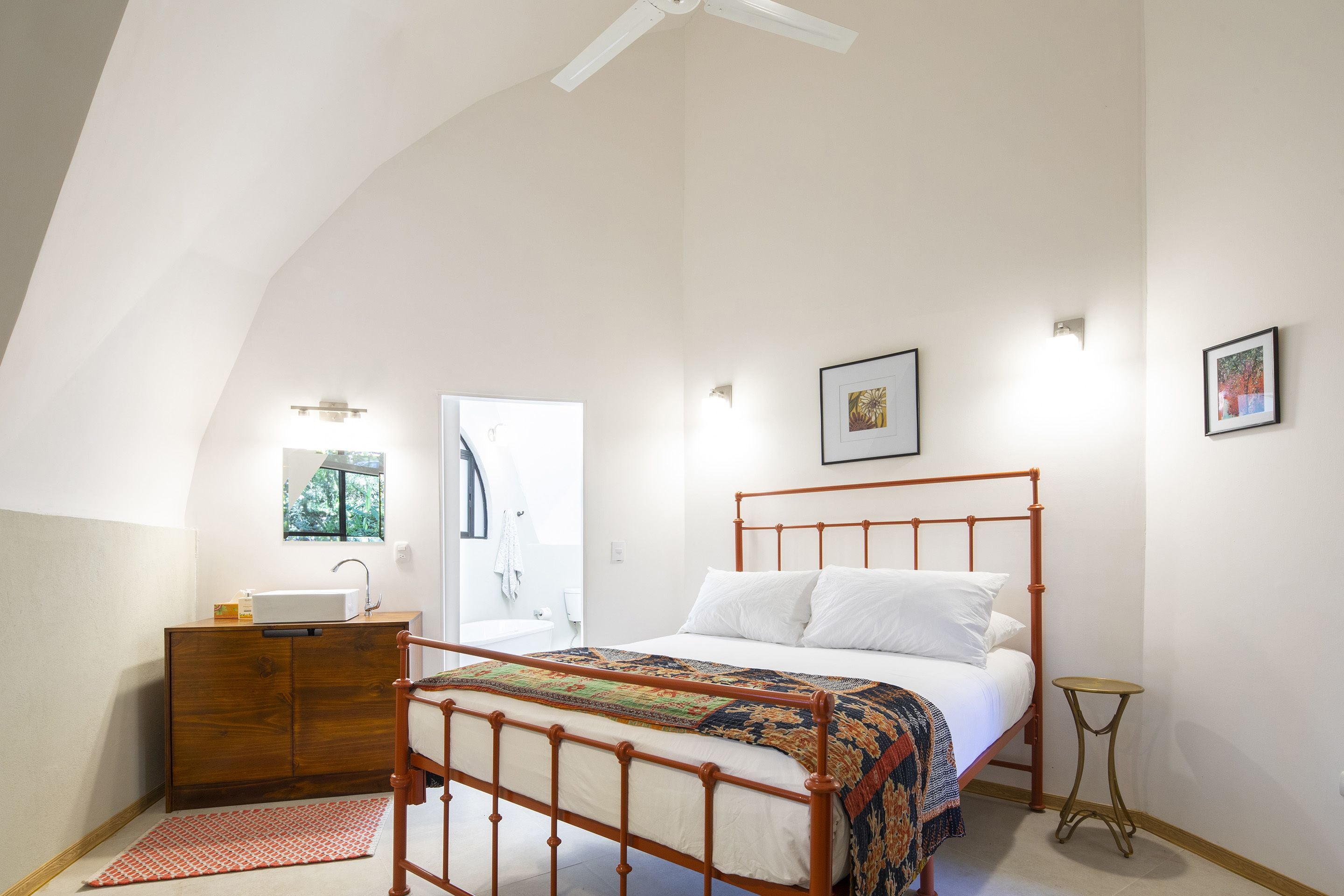 Een slaapkamer met een bed, een houten dressoir, een klein tafeltje en een raam.