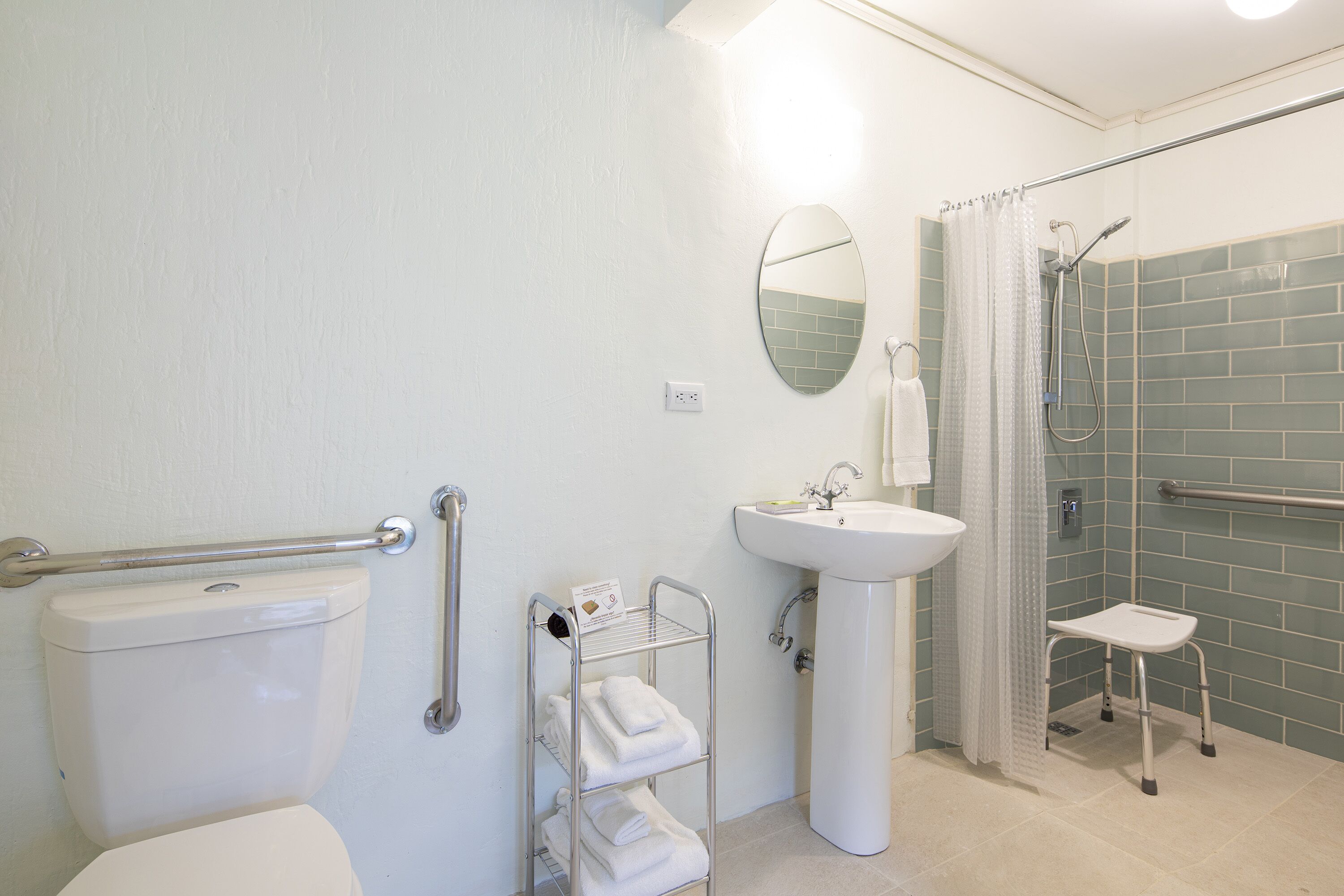A bathroom with a toilet, a sink, a shower with a grab bar, and a shelf with towels.