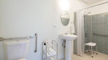 Une salle de bain comprenant des toilettes, un lavabo, une douche équipée d’une barre d’appui et une étagère avec des serviettes.