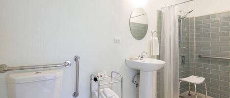 Un baño con inodoro, lavamanos, ducha con barra de apoyo y repisa con toallas.