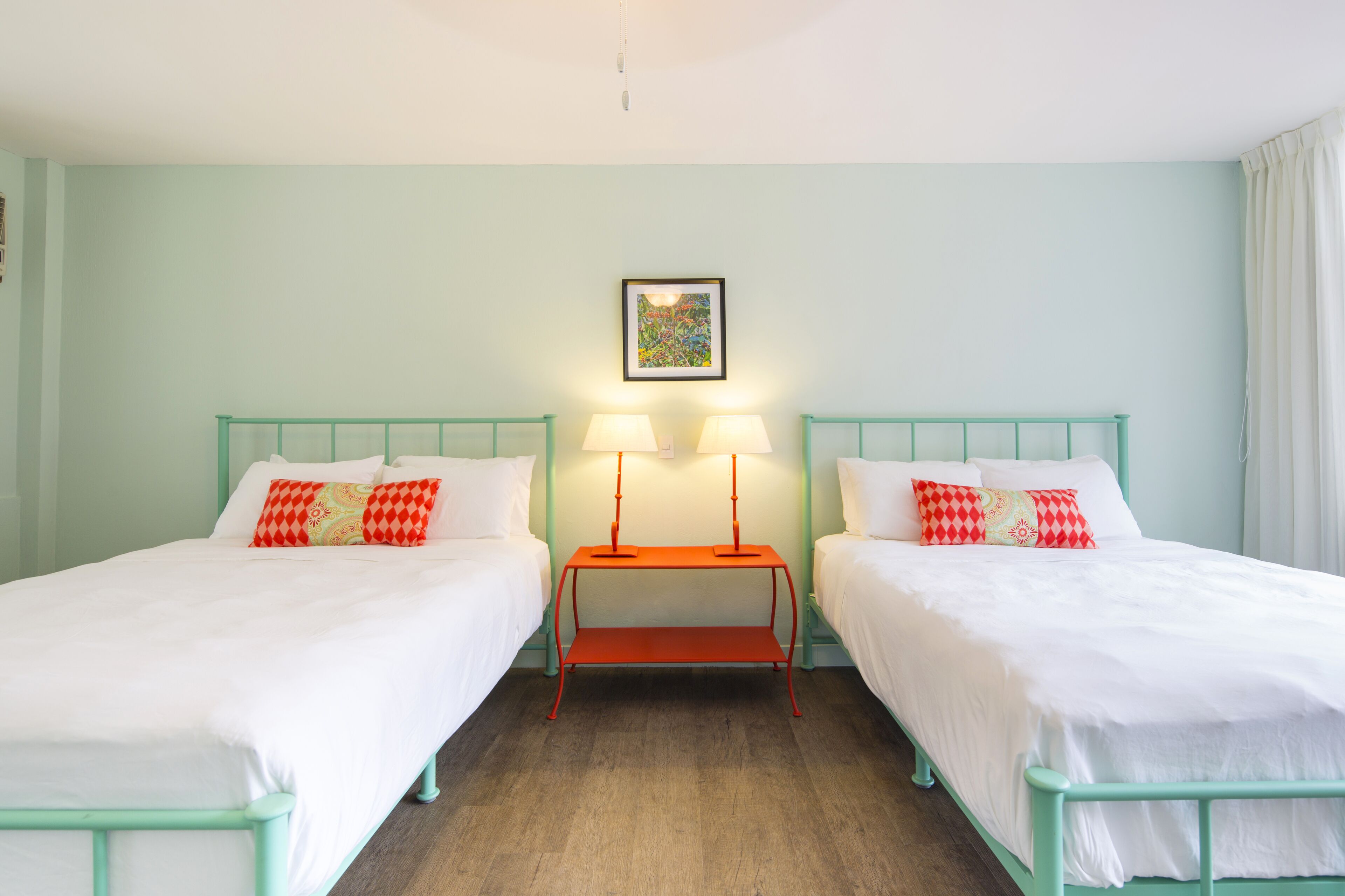 A room with two beds, a small table with lamps, and a framed picture on the wall.