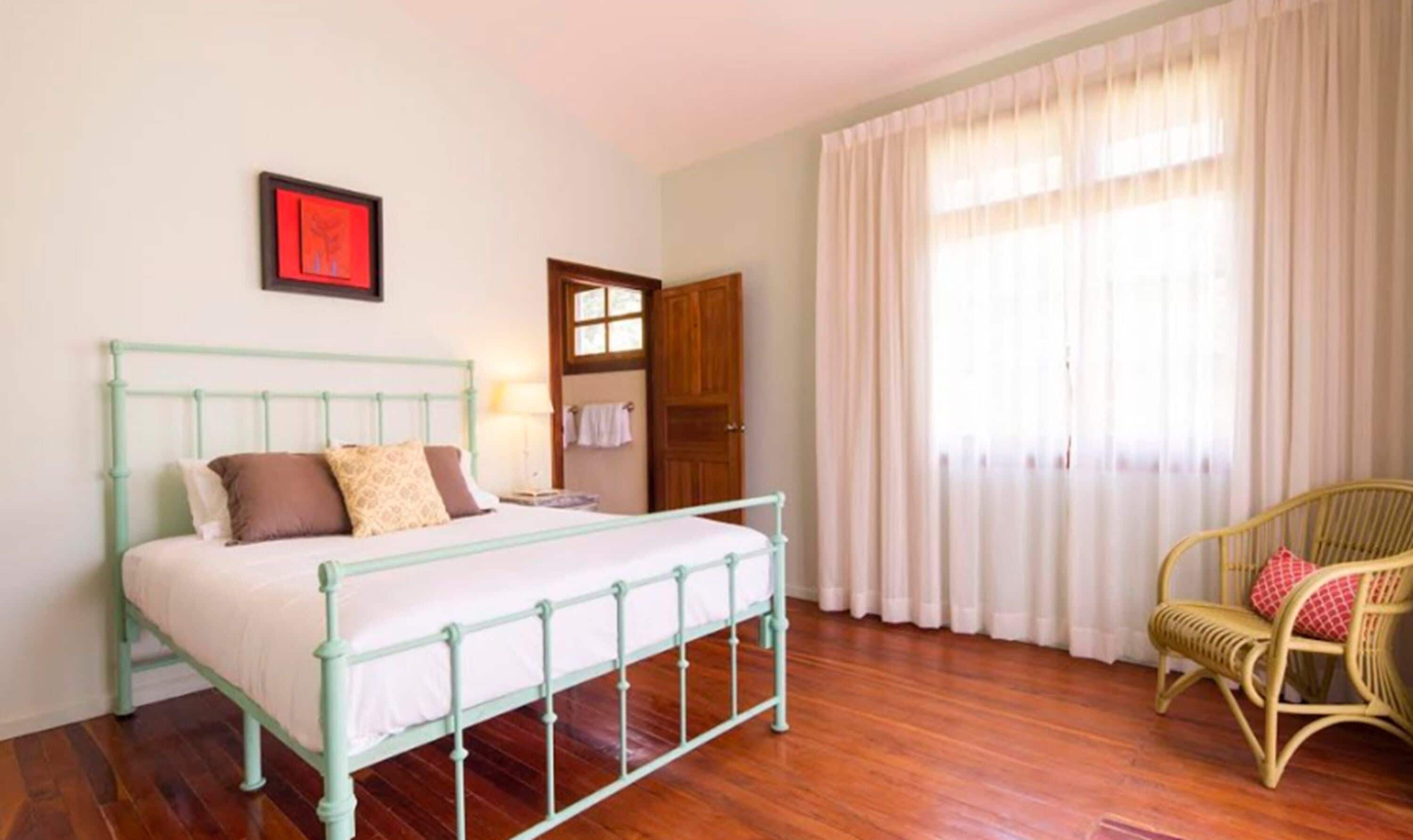 A bedroom with a bed, a chair, a door, and a window with curtains.