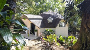 A small house with a sloped roof, surrounded by lush greenery and a variety of plants. - Villa San Ignacio (Tambor)