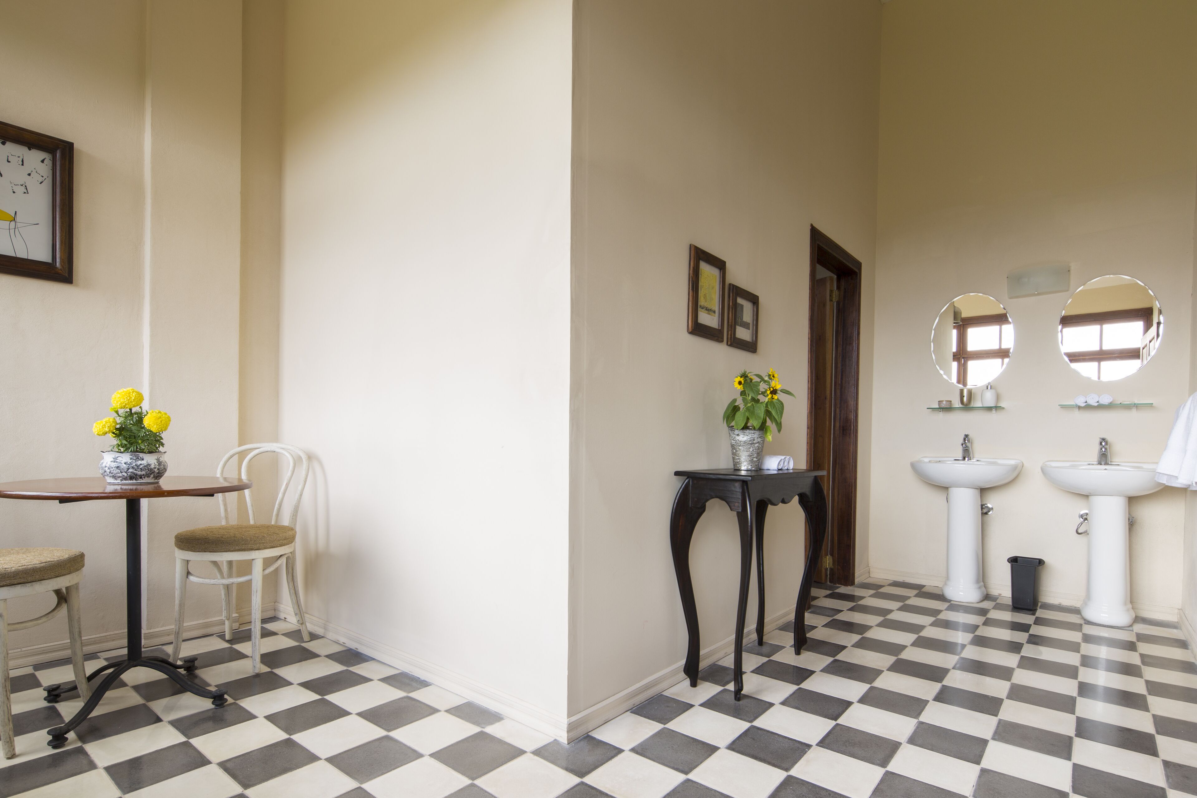 Een badkamer met een zwart-wit geruite vloer, twee wasbakken, een spiegel en een klein tafeltje met een bloevas.