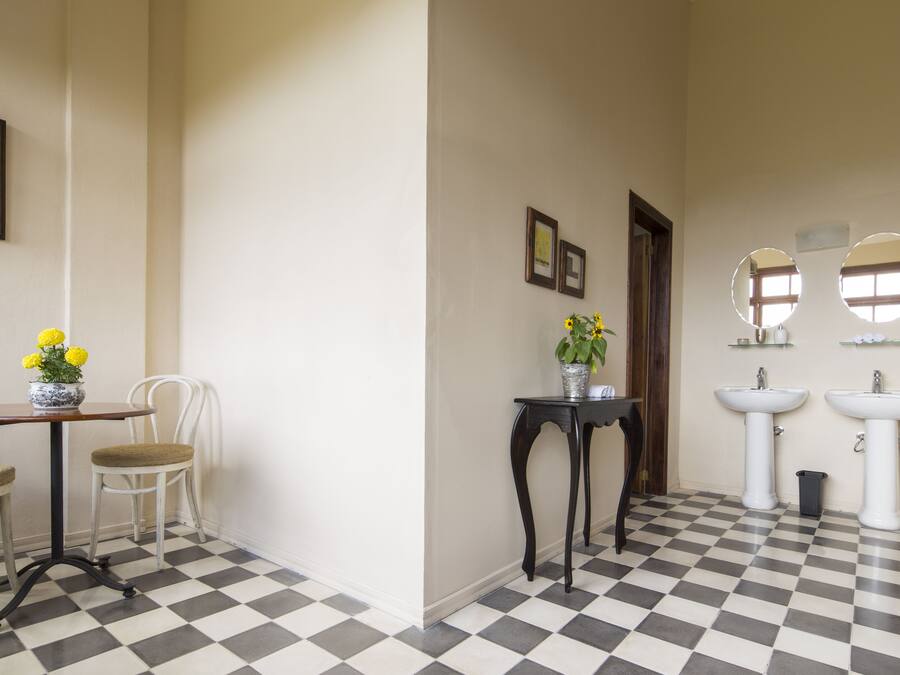Ein Badezimmer mit Schachbrettboden, zwei Waschbecken, einem Spiegel und einem kleinen Tisch mit Blumen in einer Vase.