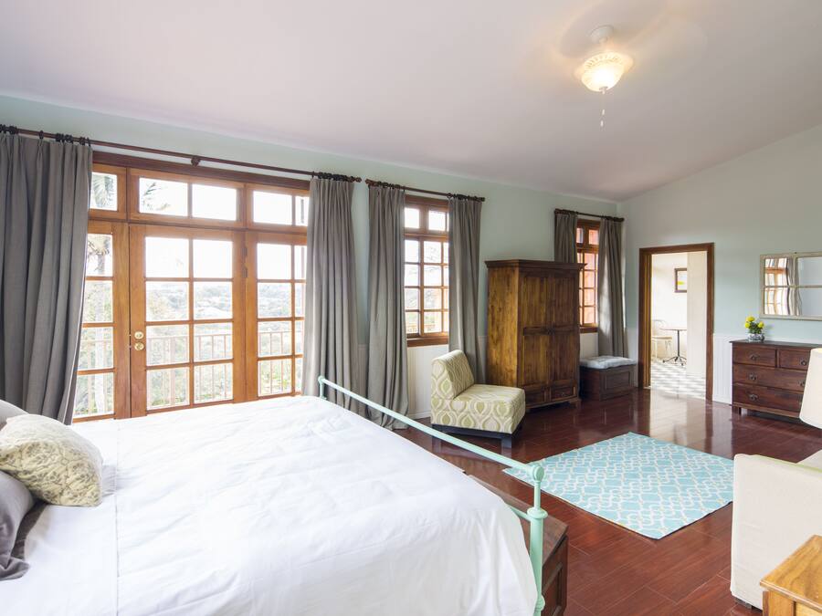 A spacious bedroom with a large bed, a wooden wardrobe, a chair, and a desk with a lamp.