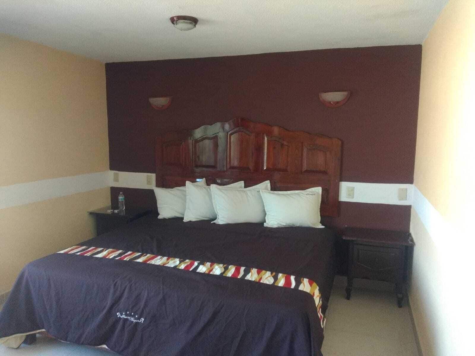 Quarto de hotel com uma cama grande, cabeceira de madeira e duas mesas de cabeceira.