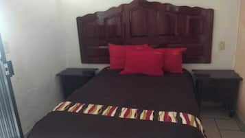 Habitación de hotel con una cama grande, un cabecero de madera, dos mesitas de noche y almohadas rojas.