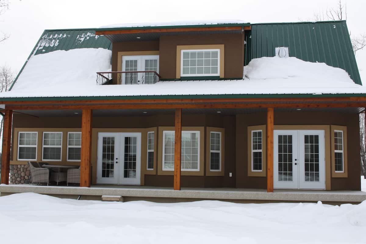 Uma casa de dois andares com varanda coberta, varanda e telhado coberto de neve.