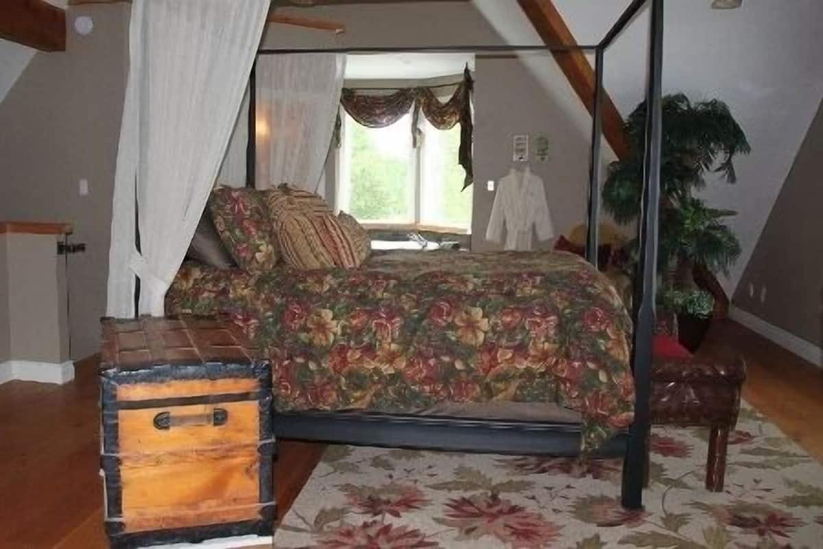 Quarto com cama de dossel, um baú de madeira e uma janela grande com cortinas.